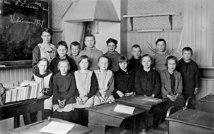 Elever som står tillsammans med fröken inuti sitt klassrum